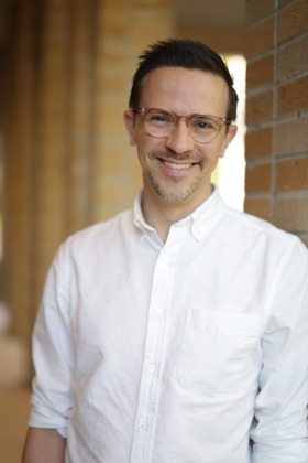 Andy Otto, smiling, in a white shirt against a brick colonnade.